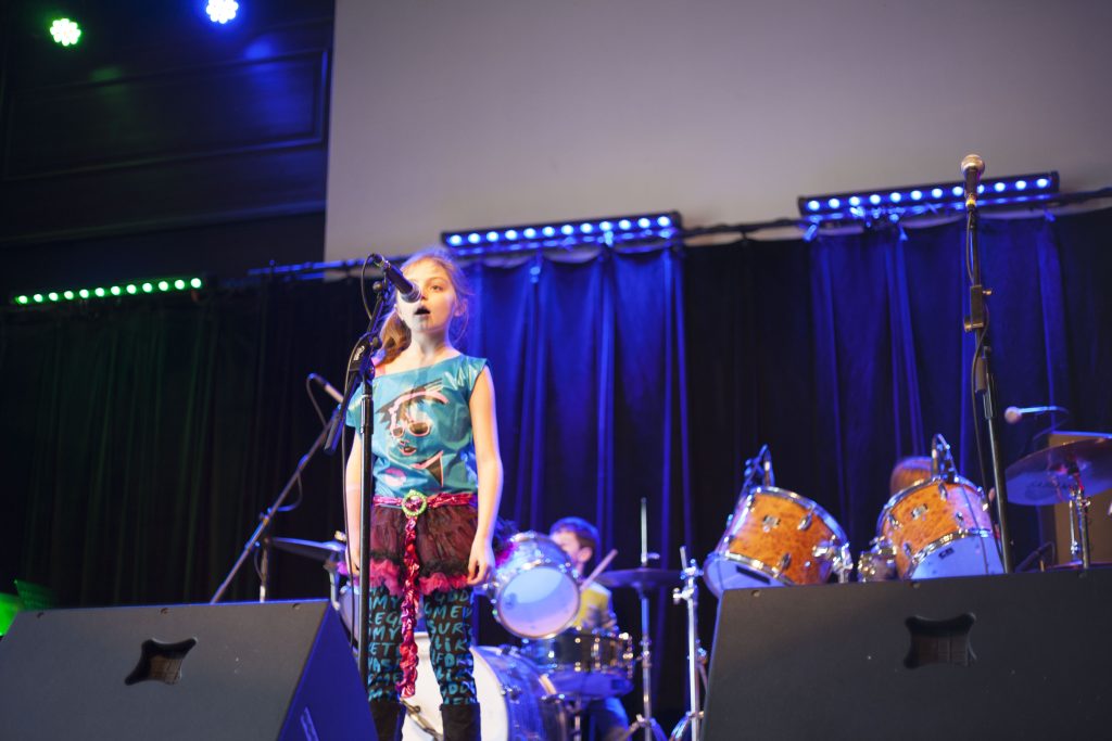 young girl on stage singing into a microphone